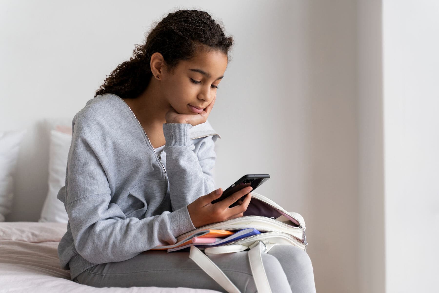 A teenage girl reading on her phone, a school bag beside her