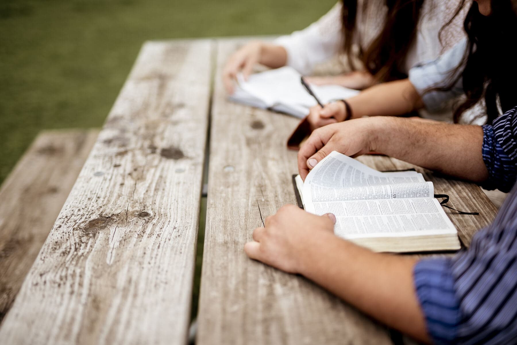 A group gathered around a long wooden table with open Bibles and notebooks