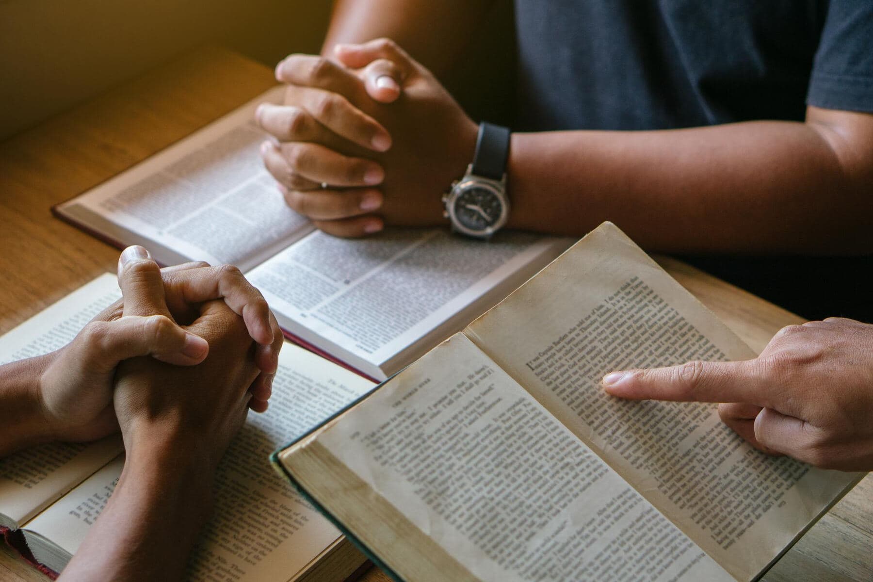 Two people's hands over an open Bible, one of them pointing at the text