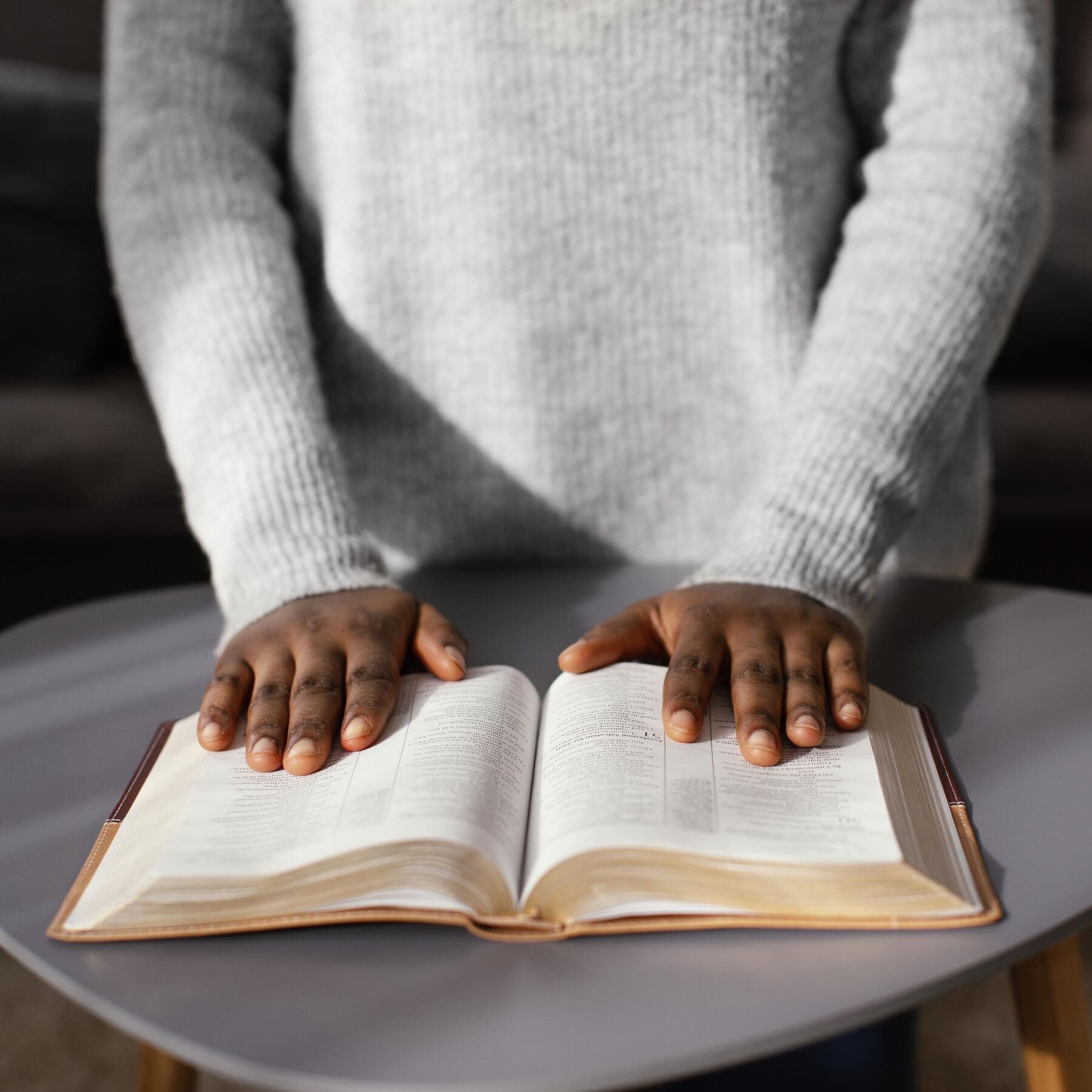A pair of hands resting on an open Bible on a table